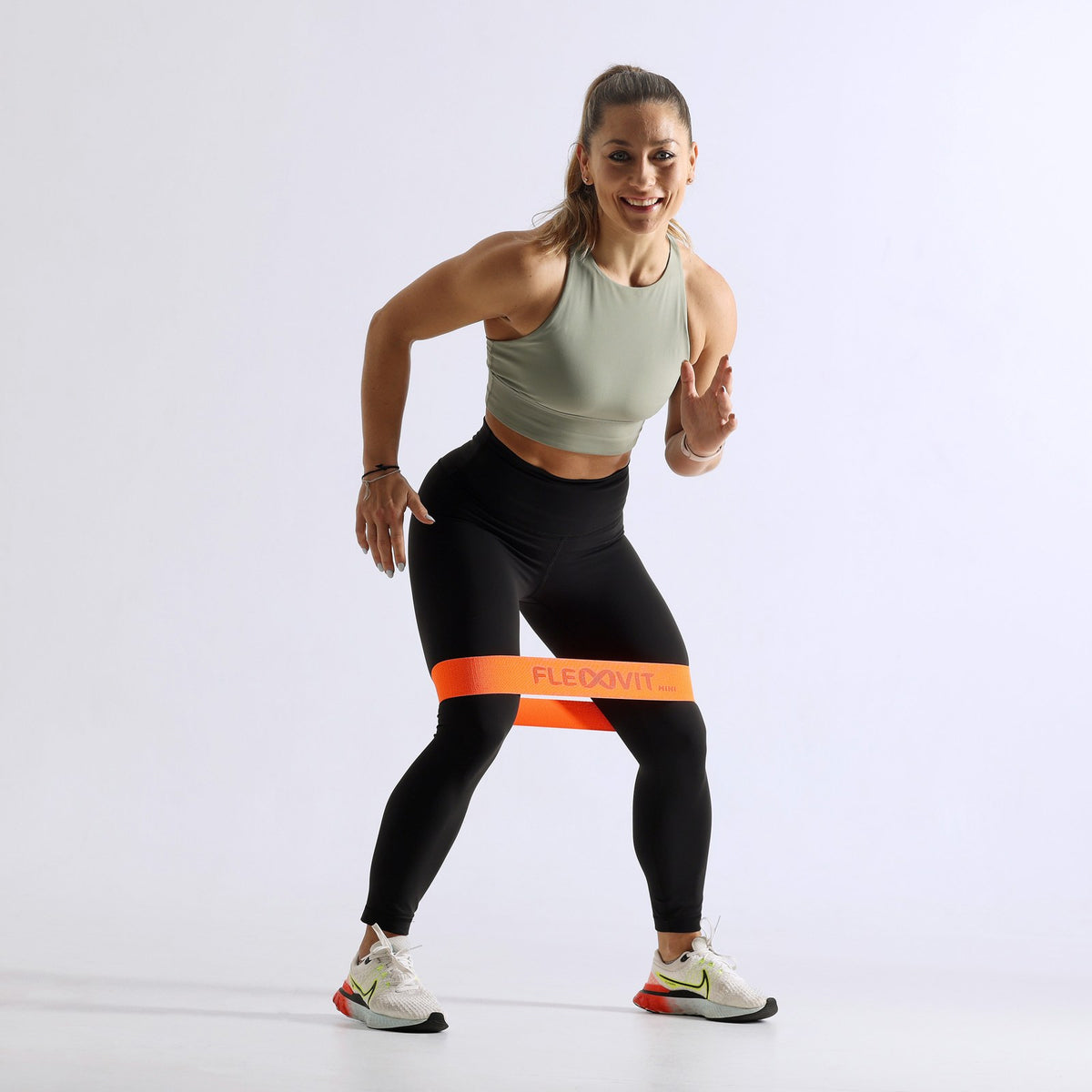 Mujer en paso lateral con una mini banda naranja sobre las rodillas, del Flexvit Mini Set de 3