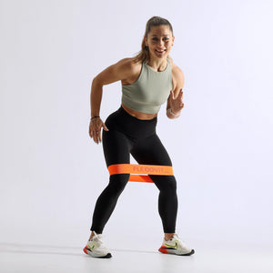 Mujer en paso lateral con una mini banda naranja sobre las rodillas, del Flexvit Mini Set de 3