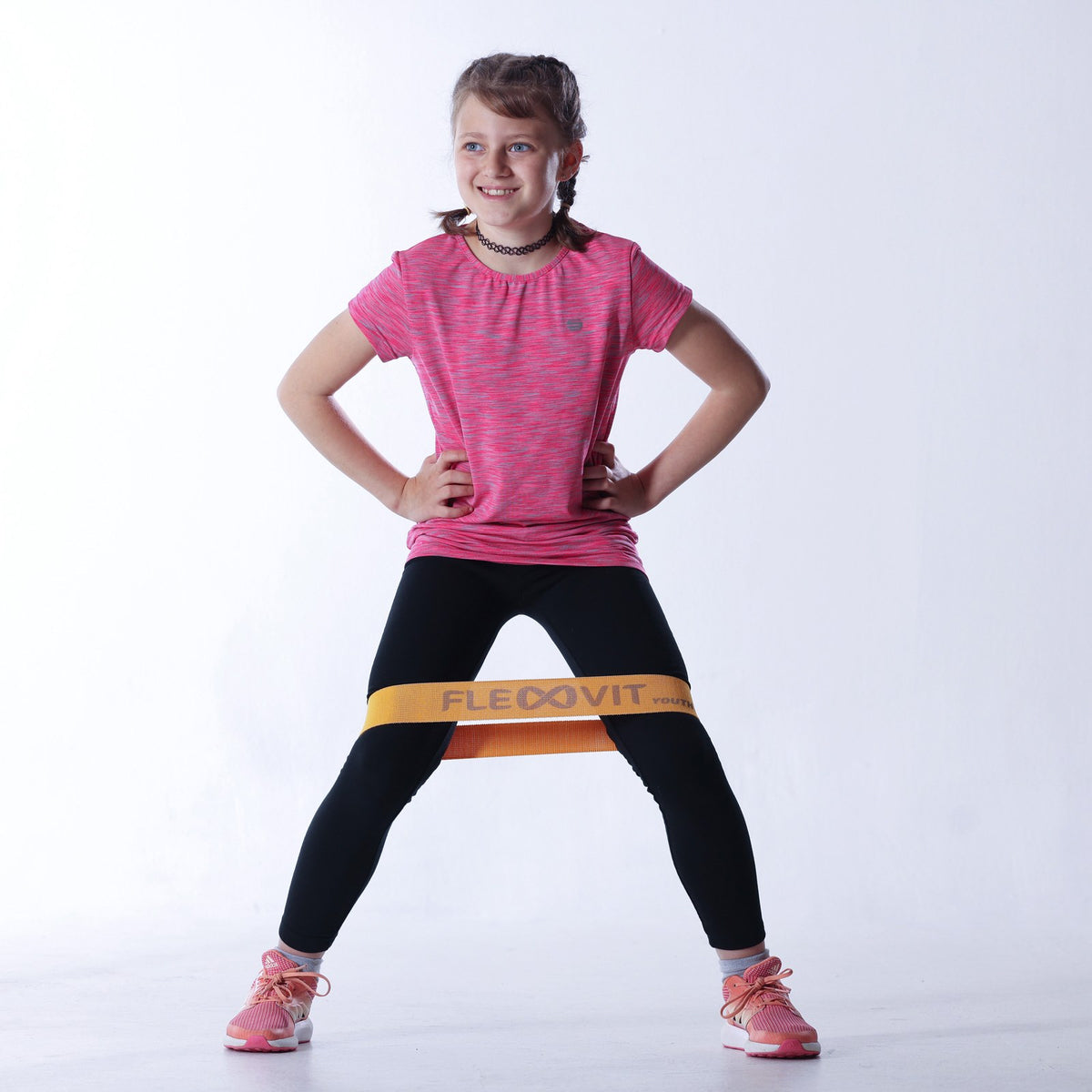 Niña de pie con las manos en la cintura y la mini banda Flexvit MinY amarilla sobre los muslos