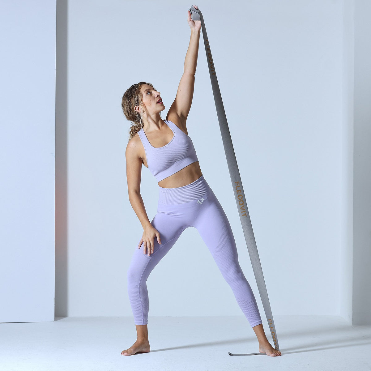 Mujer estira un brazo hacia arriba con la banda gris Flexvit NeuroBand sujeta bajo el pie