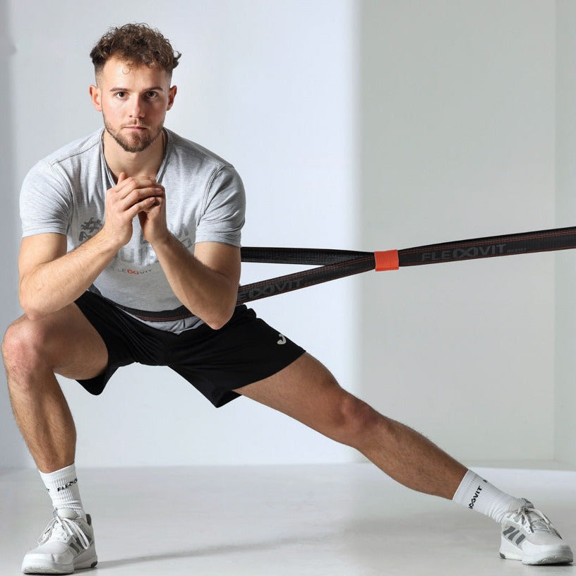 Hombre en zancada lateral con las manos juntas y la banda Flexvit Resist atada a la cintura, entrenamiento atlético